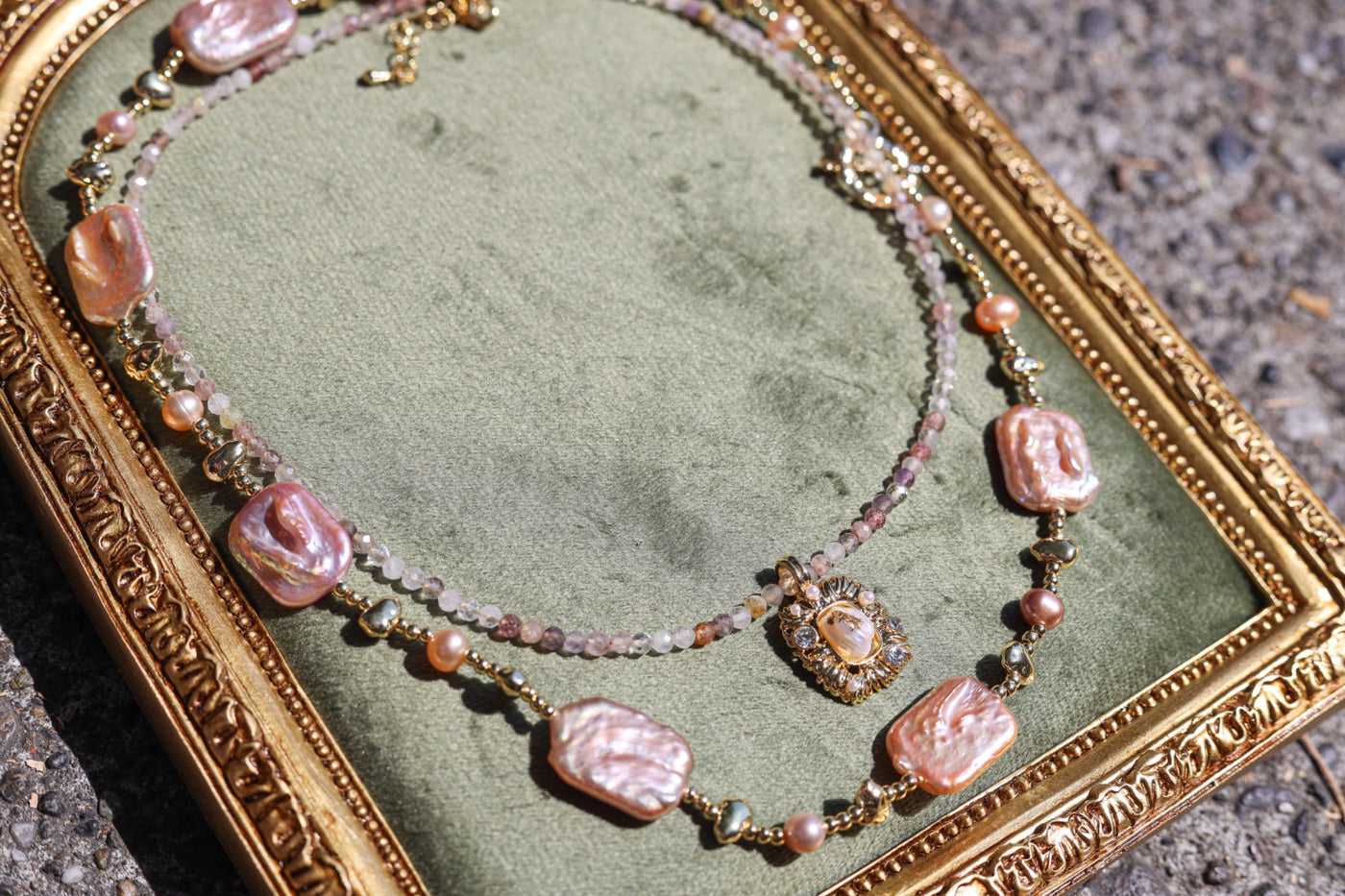 Pink pearl and gemstone necklaces arranged on green velvet in a vintage gold frame