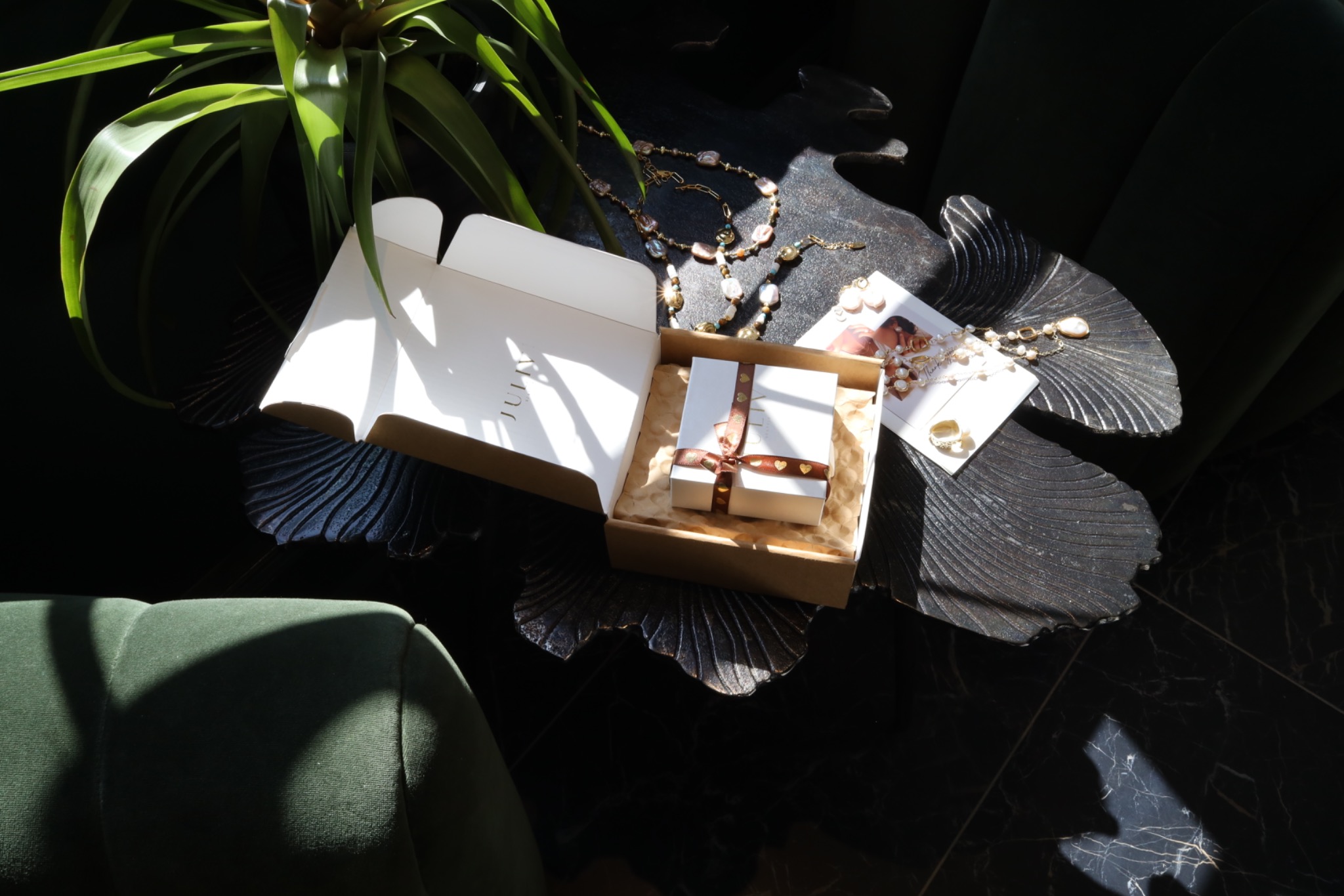 JULIV packaging with a ribbon-tied jewelry box inside an open mailer, surrounded by pearl jewelry