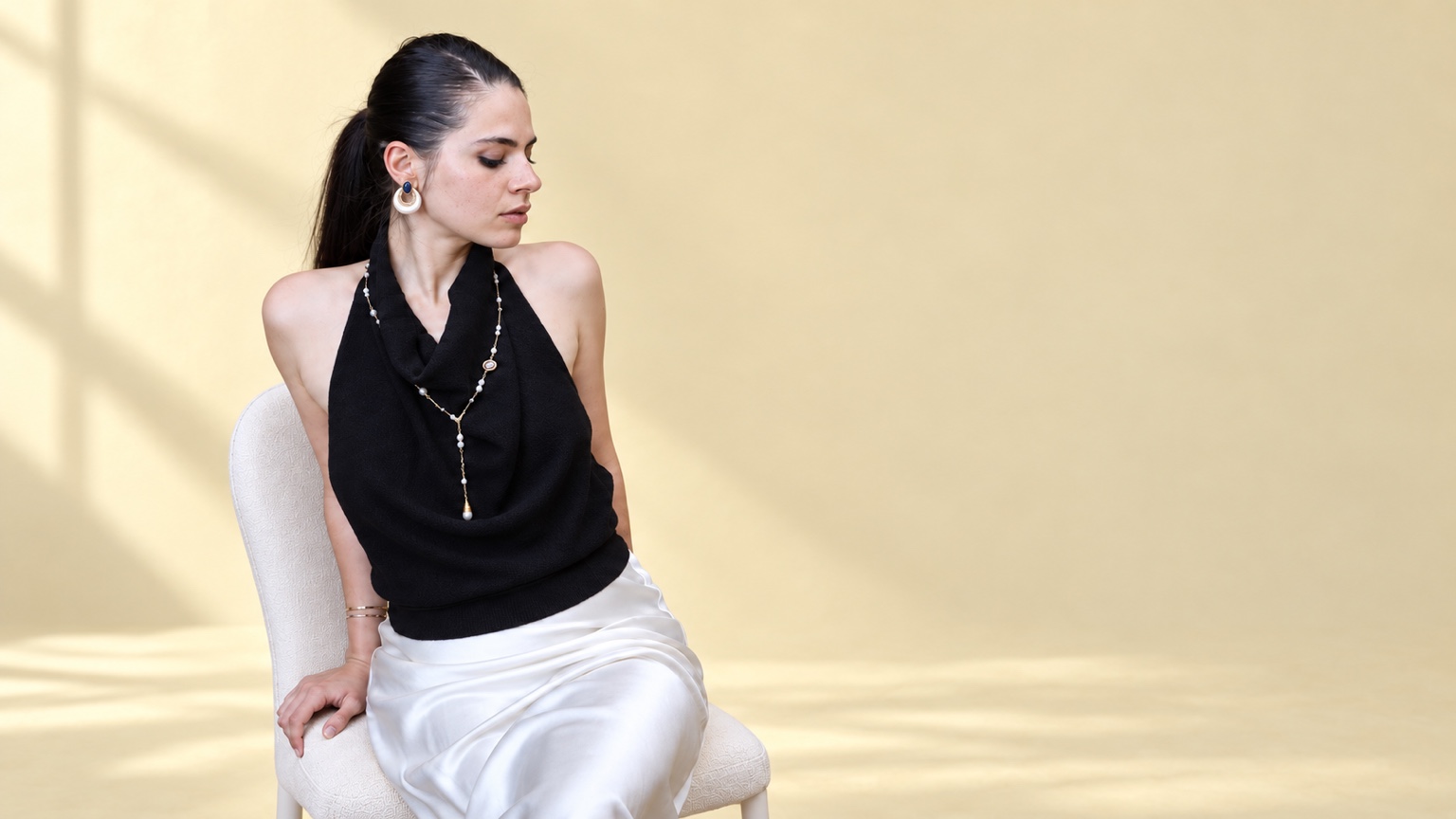 JULIV’s founder wearing a pearl lariat necklace with a black halter top against a soft yellow backdrop